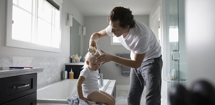 Père qui coiffe sa fille dans une salle de bain